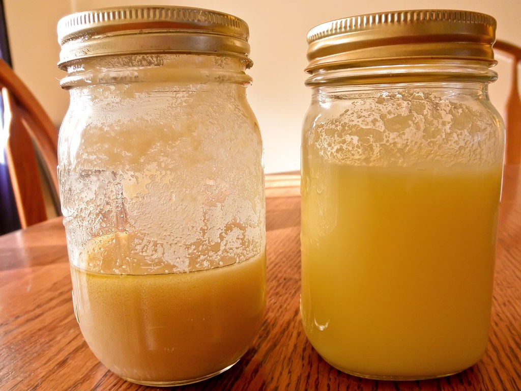 Two glass jars on a wooden table, one containing solidified fat and the other liquid fat, both with a yellowish tint.