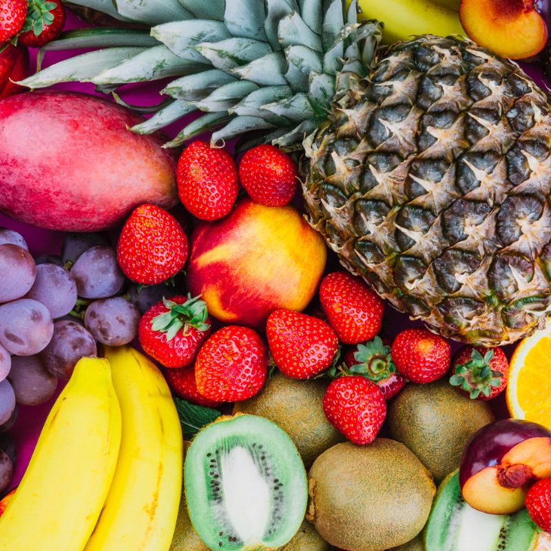 A variety of fruits including pineapples, strawberries, mangoes, bananas, grapes, kiwis, and oranges, arranged together.