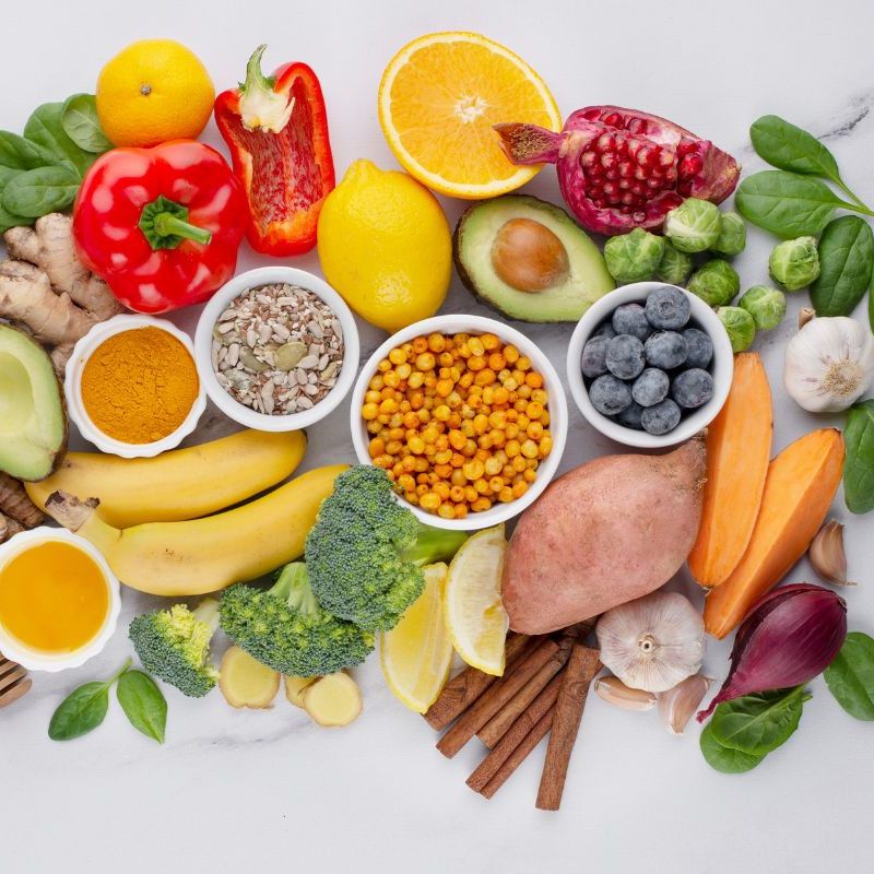 A variety of fresh and healthy foods including fruits, vegetables, seeds, and spices arranged neatly on a white surface.