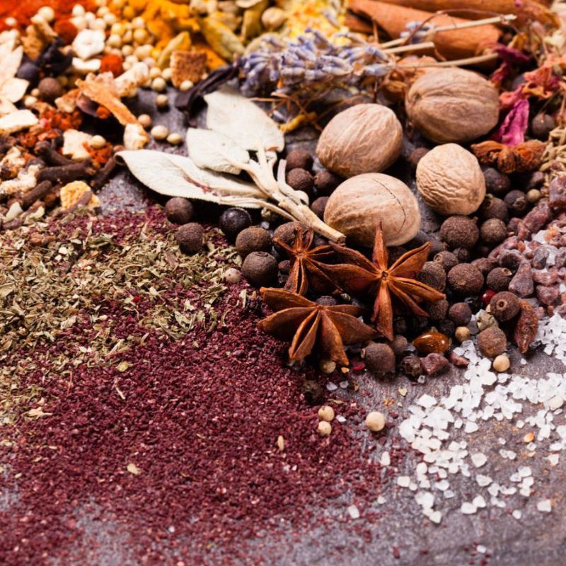 A variety of spices and herbs, including star anise, dried leaves, nuts, and peppercorns, set against a textured surface—ideal for those exploring gut health supplements.