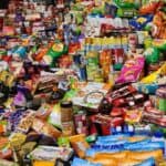 A cluttered assortment of various packaged food products, including snacks, canned goods, cereals, and beverages, is piled on shelves and a counter. Among them are some of the best probiotics for gut health, perfect for those looking to hack your health: the secrets of your gut.