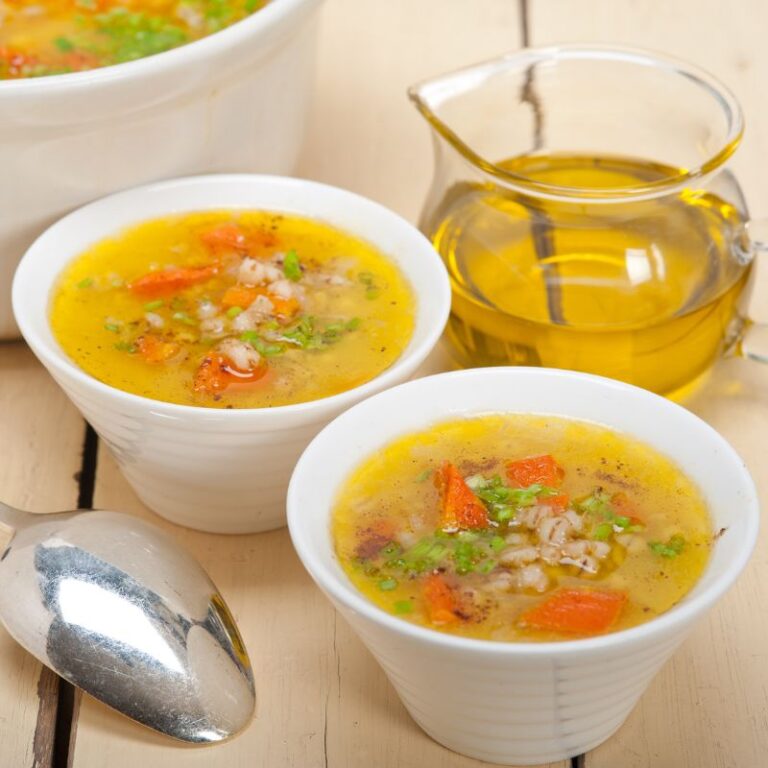 two white bowls of gut healing garlic ginger soup and a jug of oil