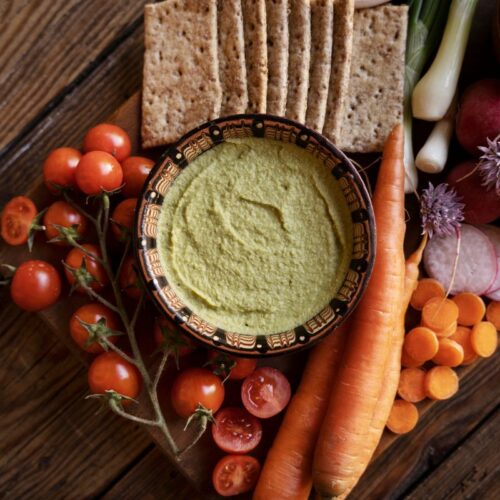 candida-friendly zucchini dip recipe in a bowl surrounded by vegetables, carrots, tomatoes and crackers
