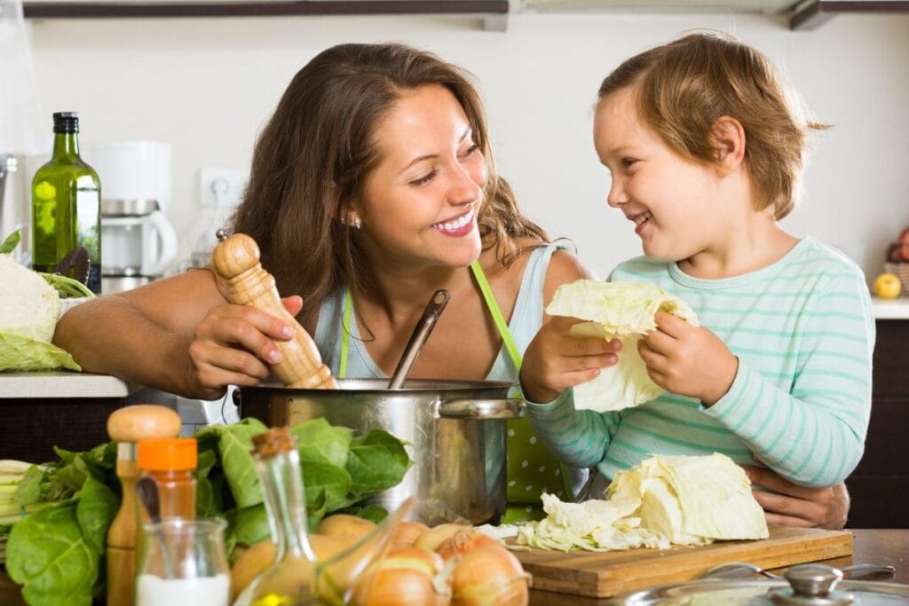 A smiling woman and child preparing food together in a kitchen.