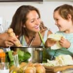 A smiling woman and child preparing food together in a kitchen.