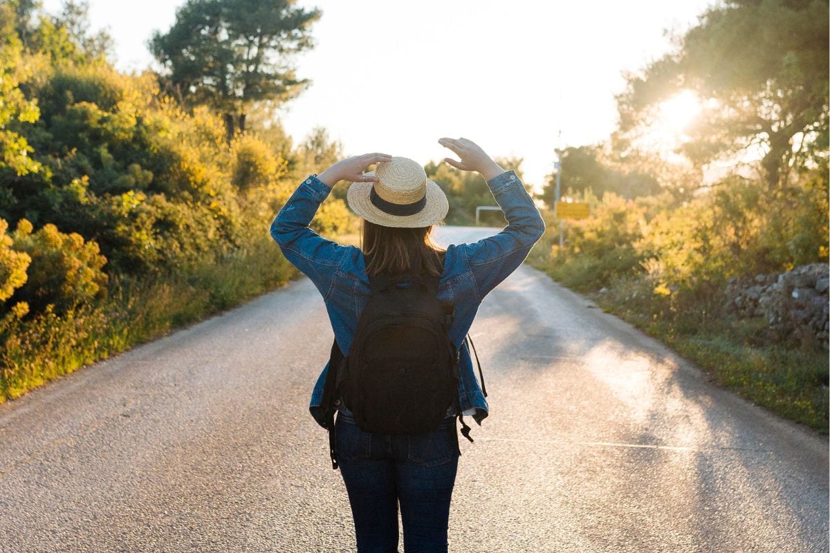 Person holding onto a hat while walking on a rural road during sunset.