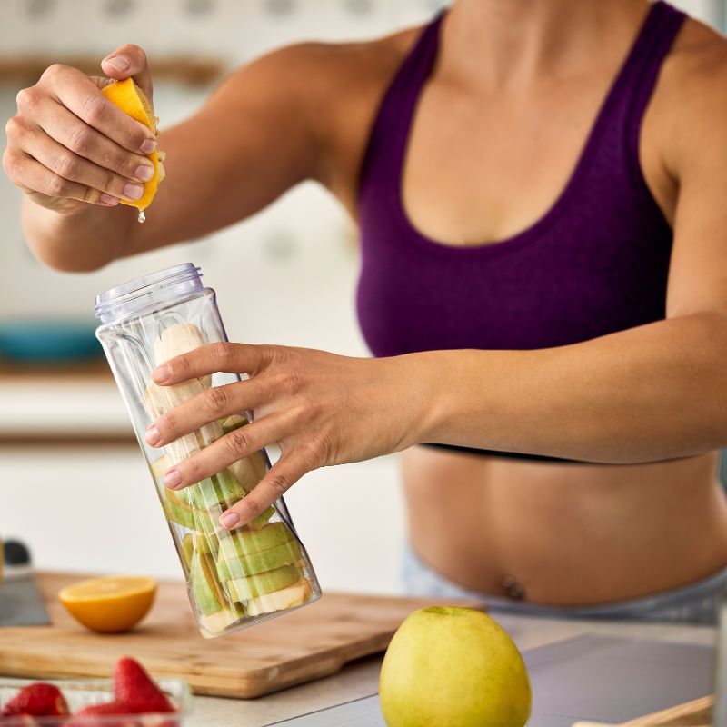 A woman in a sports bra preparing an anti-candida diet recipe over a kitchen counter with fruits around.