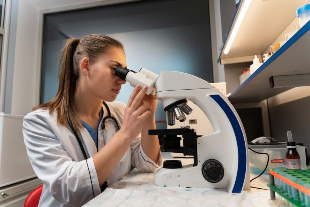 A female scientist in a lab coat using a microscope in a laboratory setting.