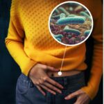 Person in a yellow sweater and jeans with a graphical insert showing bacteria, implying a focus on gut health or microbiology.