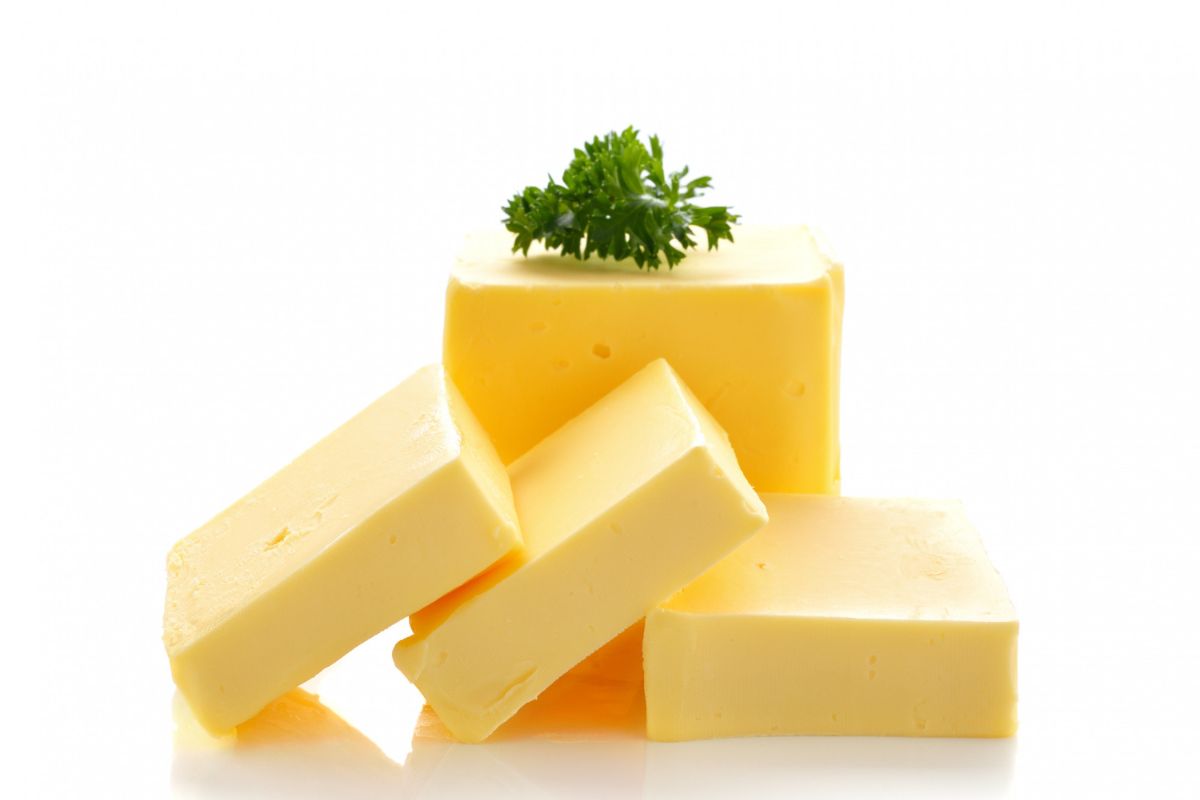 Sliced yellow cheese blocks and pieces with a parsley garnish on a white background.