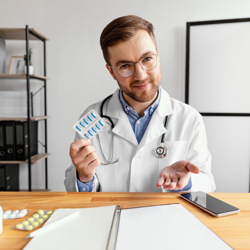 A male doctor in a white coat holding a dna model, smiling at the camera in an office setting.
