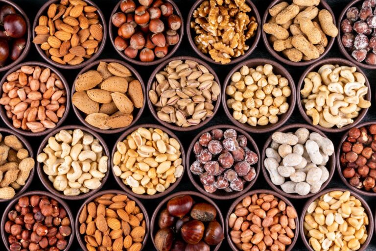 A variety of nuts and seeds displayed in small bowls, including almonds, hazelnuts, walnuts, peanuts, pistachios, cashews, and chestnuts.