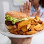 A person gestures to decline a plate of hamburger and potato wedges being offered to them.