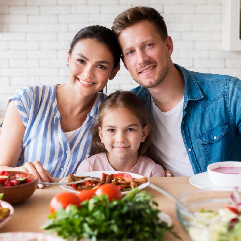 A woman, man, and young girl sit together at a table with a variety of dishes, smiling at the camera.