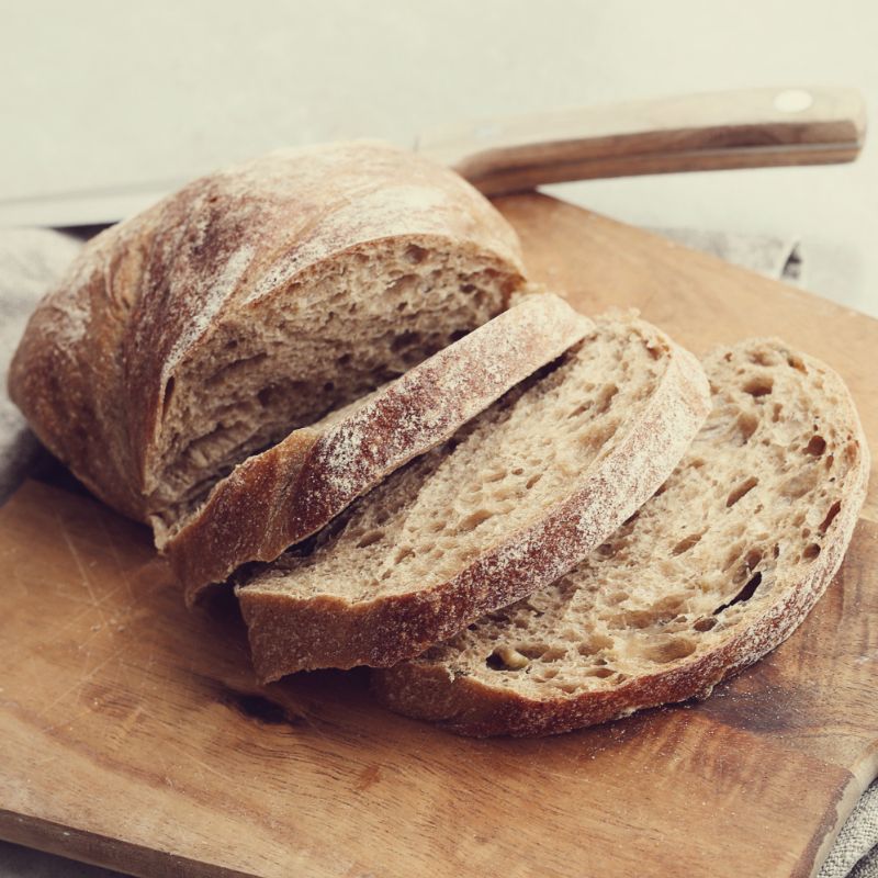 Sliced loaf of rustic bread on a wooden cutting board next to a knife.
