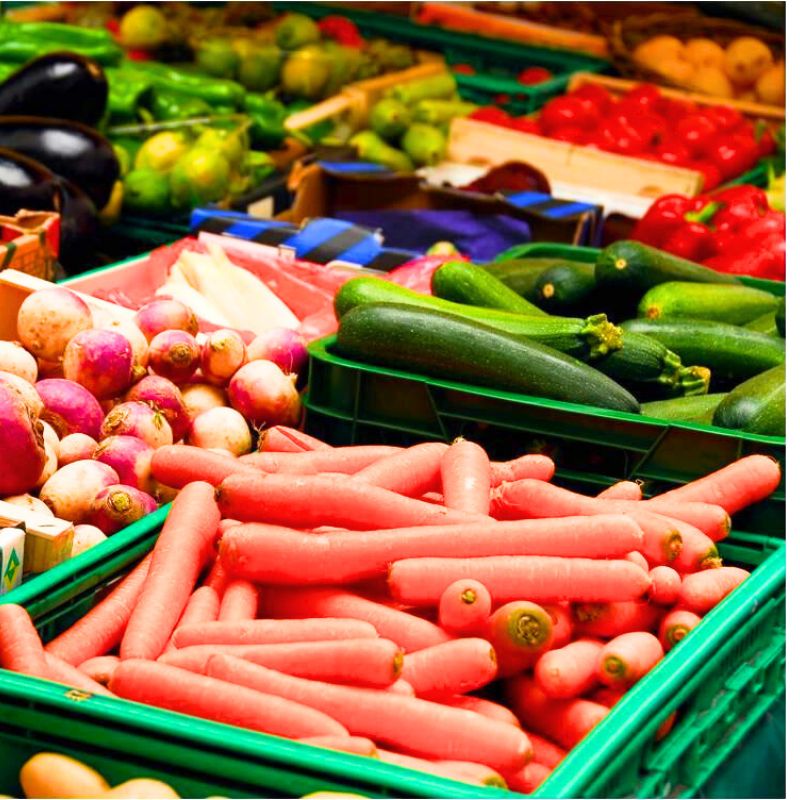 Various fresh vegetables including carrots, zucchinis, turnips, eggplants, and tomatoes are displayed in green crates at a market—ideal for those on an anti candida diet.