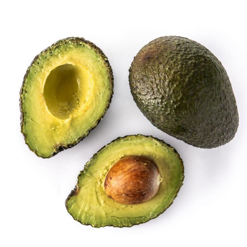 A whole avocado next to two avocado halves, one with a pit and one without, showcases an ideal choice for the anti Candida diet on a pristine white background.