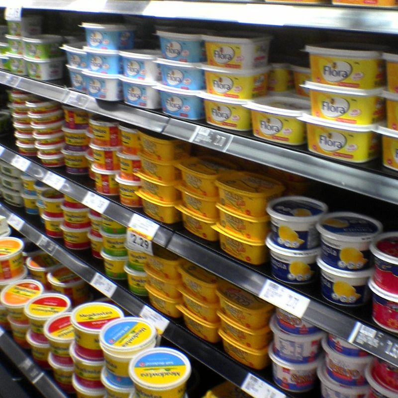 Shelves in a grocery store display various brands and types of margarine and butter in plastic tubs, highlighting the essential oils and fats that play crucial roles in our bodies.