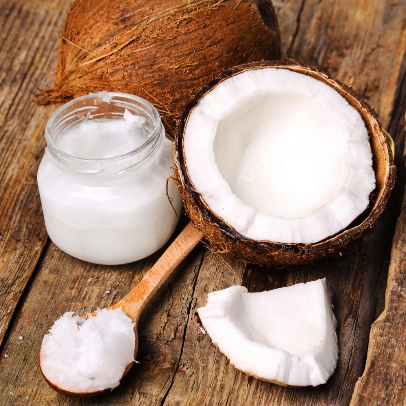 Halved coconut, coconut oil in a jar, and a wooden spoon with coconut oil on a rustic wooden surface highlight the rich benefits of fats and oils. These natural sources underscore the vital functions of fats and oils in the body for energy storage and nutrient absorption.