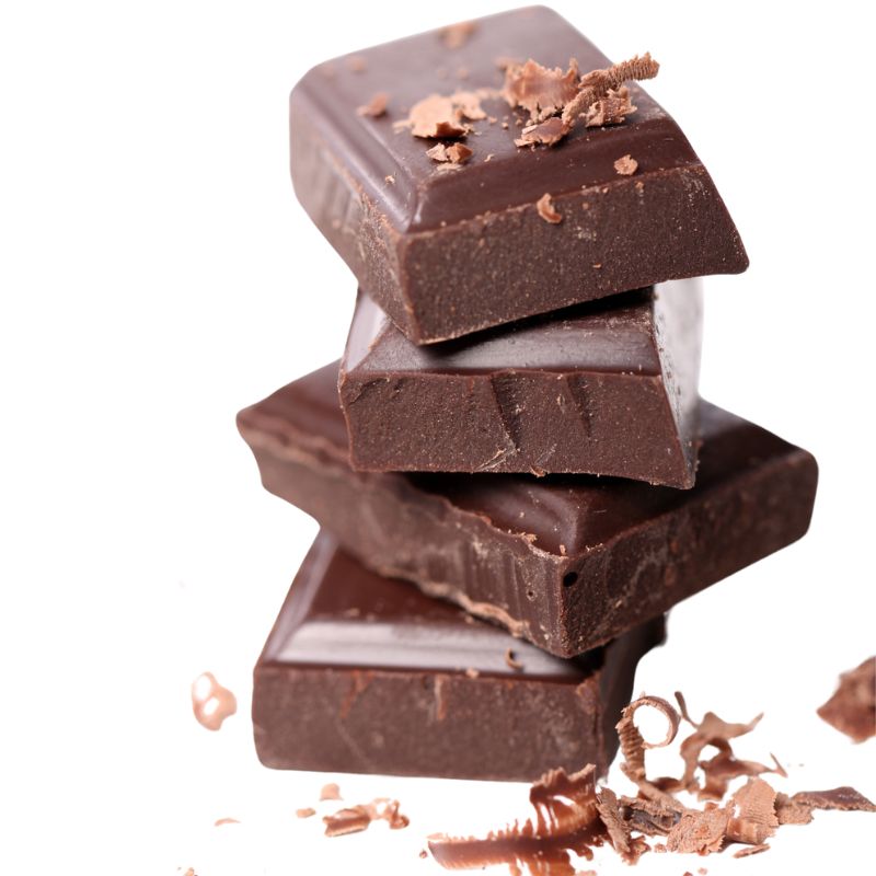Stack of four dark chocolate pieces with chocolate shavings scattered around them against a white background.