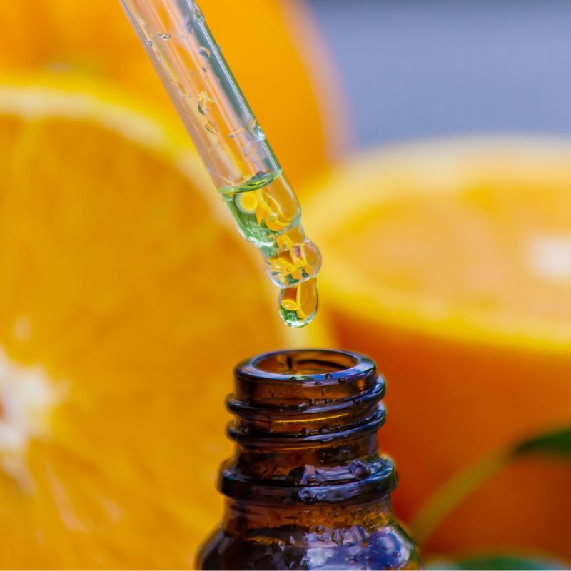 A dropper dispensing liquid into a brown glass bottle. Slices of orange are in the background.