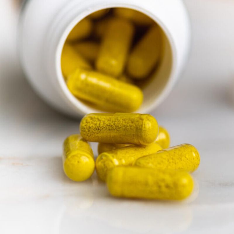 A scattered pile of yellow berberine capsules spills out from a tipped-over white plastic bottle onto a smooth surface.