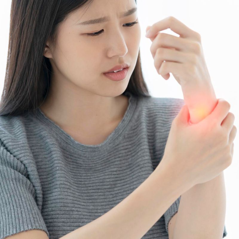 A woman wearing a gray shirt holds her wrist, which is glowing red, indicating pain or injury. Considering her discomfort, she might benefit from consuming anti-inflammatory foods to help reduce the inflammation.