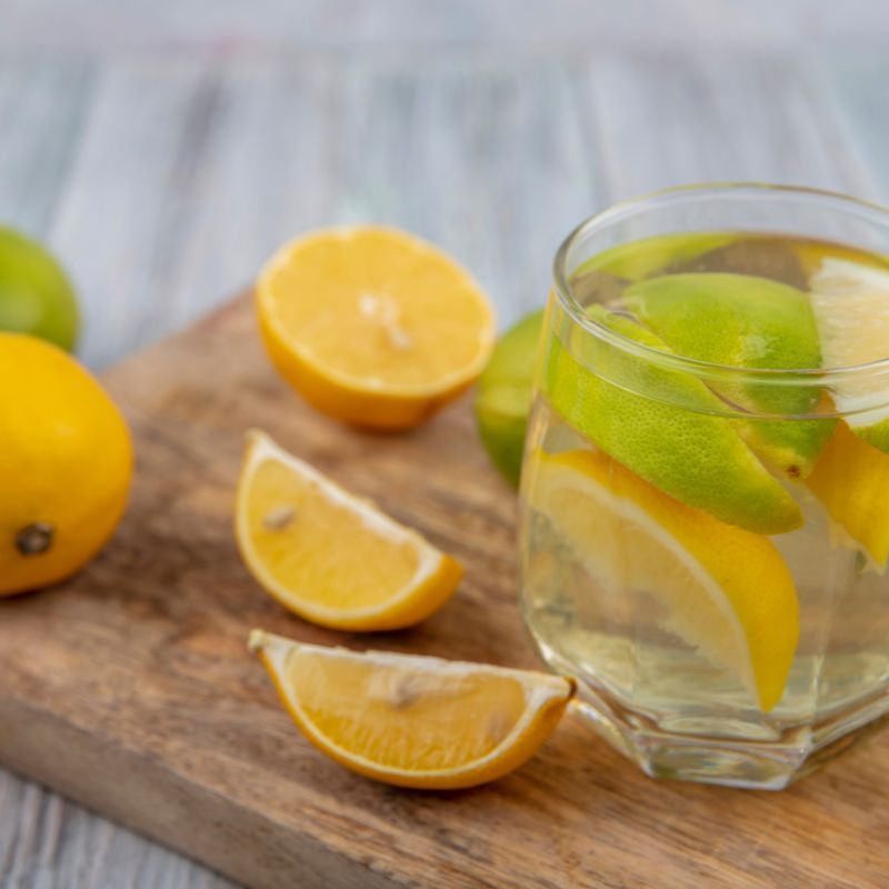Glass of alkalised water with fresh lemon slices on a wooden cutting board, surrounded by lemon quarters.