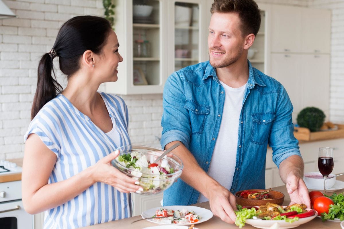 A couple preparing a meal together in a kitchen, smiling while sharing a bowl of salad.