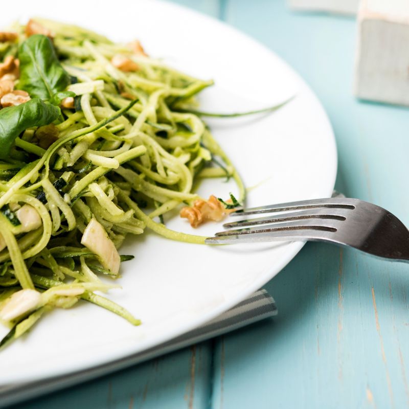 Zucchini noodles with tahini lemon dressing served on a white plate with a fork, set on a blue table — a fresh, gut-friendly meal perfect for the Candida diet.