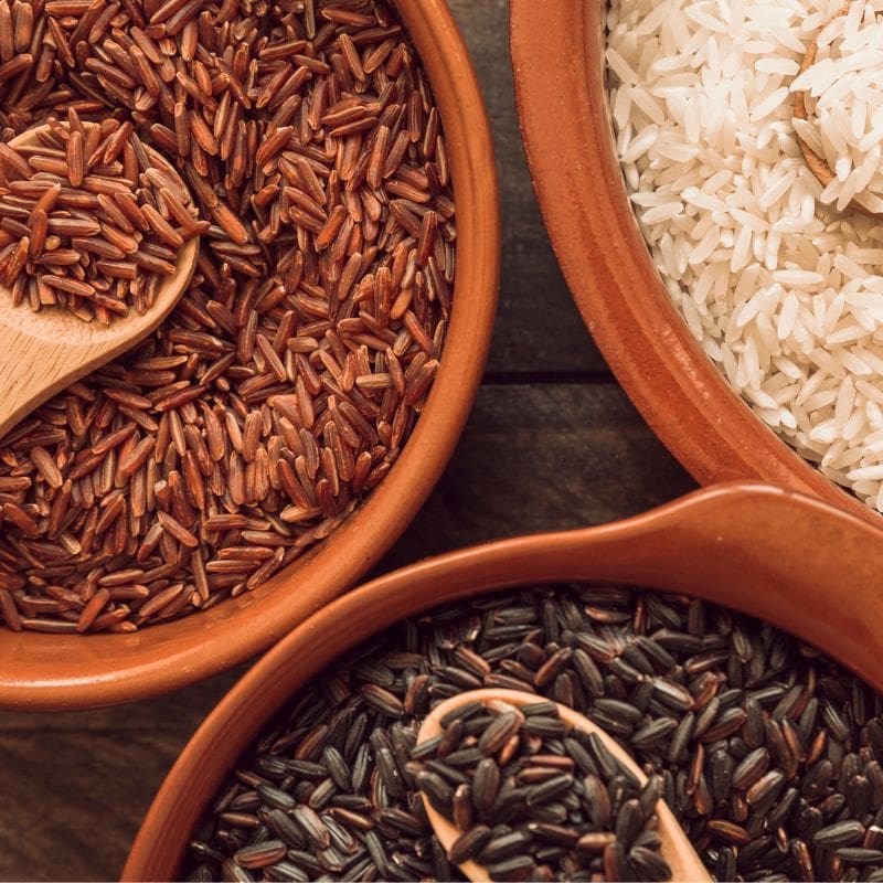Three varieties of rice in terracotta bowls with wooden spoons.