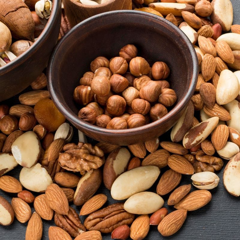 A variety of mixed nuts spilling out from a wooden bowl.