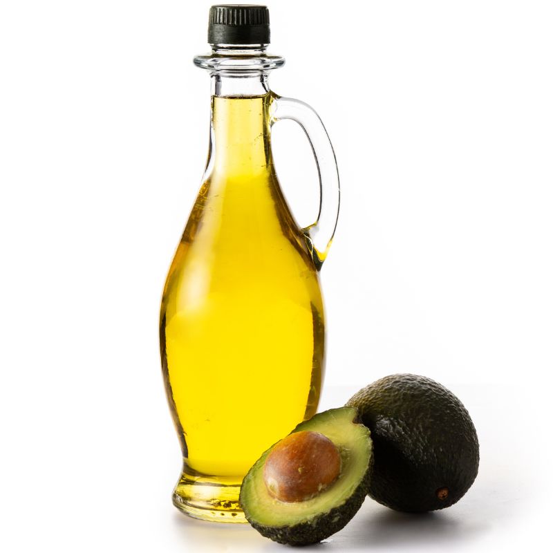 Glass bottle of oil with whole and halved avocado on a white background.