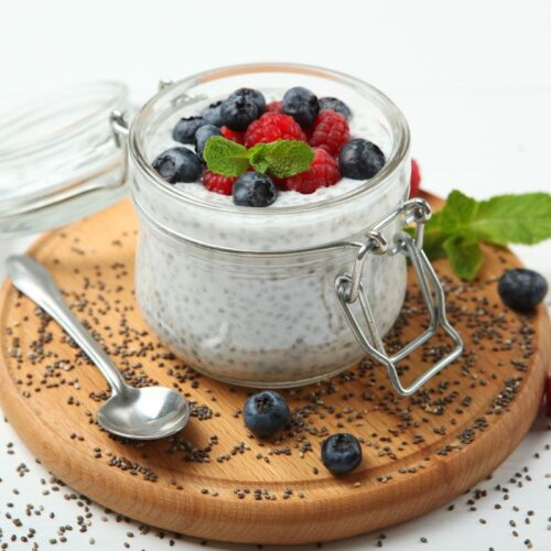 small jar of coconut yogurt with chia, flax and cinnamon sits on a wooden cutting board with a teaspoon resting beside it