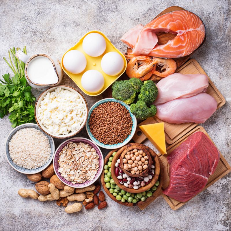 A variety of foods including eggs, chicken, salmon, shrimp, beef, cheese, broccoli, chickpeas, nuts, rice, oats, and lentils displayed on a gray surface. They have all earnt a place on the candida diet food list