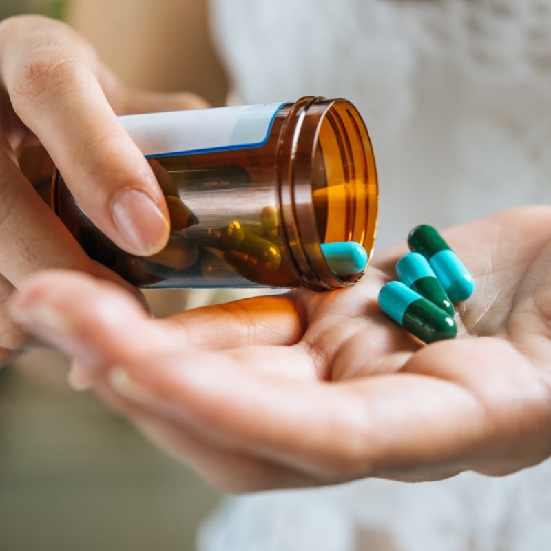 A person pouring capsules from a prescription bottle into their hand.