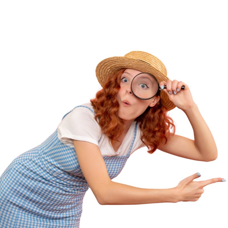 A woman wearing a straw hat and a blue checkered dress holds a magnifying glass to her eye and points with her finger while making an exaggerated facial expression.