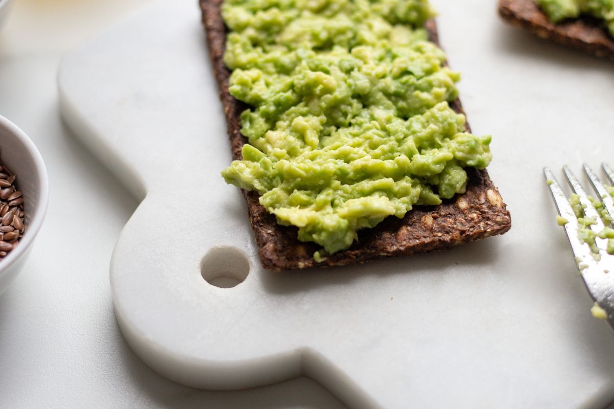 smashed avocado on seed crackers rest on a white marble cutting board