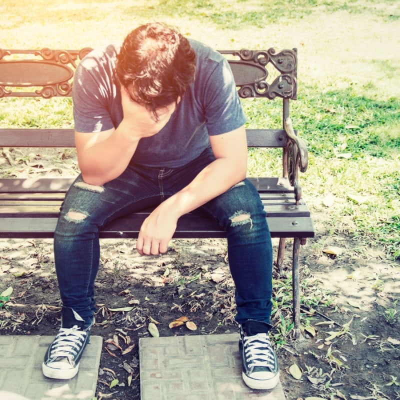 A person sitting on a park bench, looking distressed with their head in their hand.