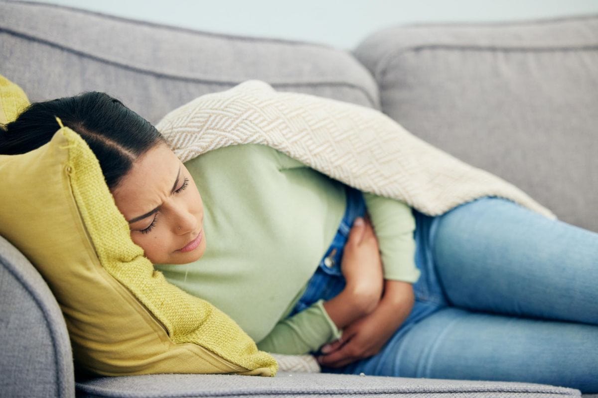 A woman resting on a couch, appearing uncomfortable or in pain, holding her abdomen.