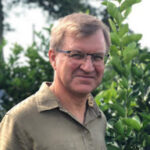 Man with glasses smiling outdoors.