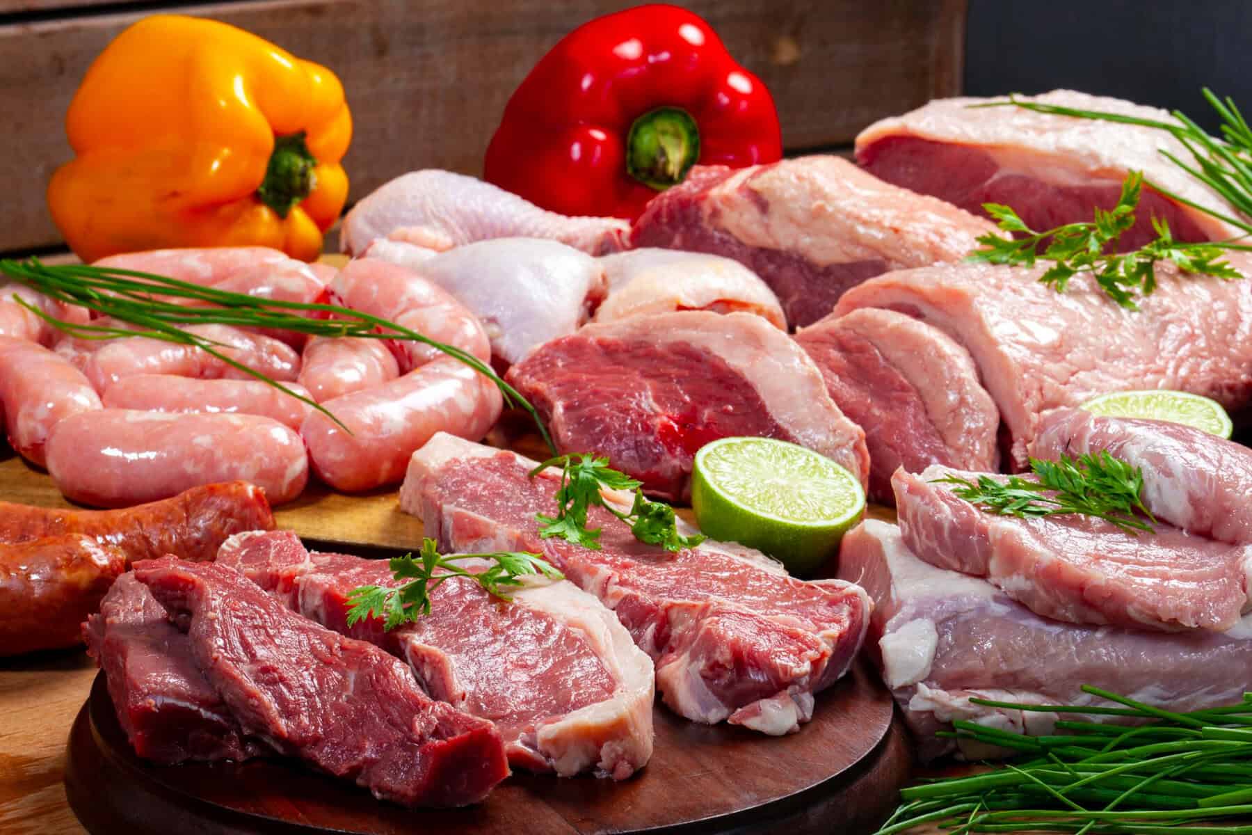 Different kinds of red meat on a stainless steel tray, including beef, pork, lamb and chicken.